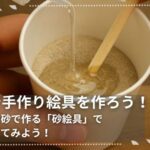 紙コップに入った細かい砂にアラビアゴムメディウムを加え、割りばしで混ぜて絵具を作っている様子。“家族で手作り絵具を作ろう！思い出の砂で作る『砂絵具』で絵を描いてみよう！”というメッセージ入り。